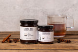 Two jars of Laurel Hill Chia Tea Jelly spread on a rustic wooden table, with a glass mug of tea and star anise in the background.