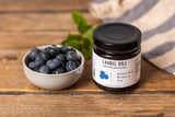 Laurel Hill blueberry jam styled with a bowl of fresh blueberries on a rustic wood table.